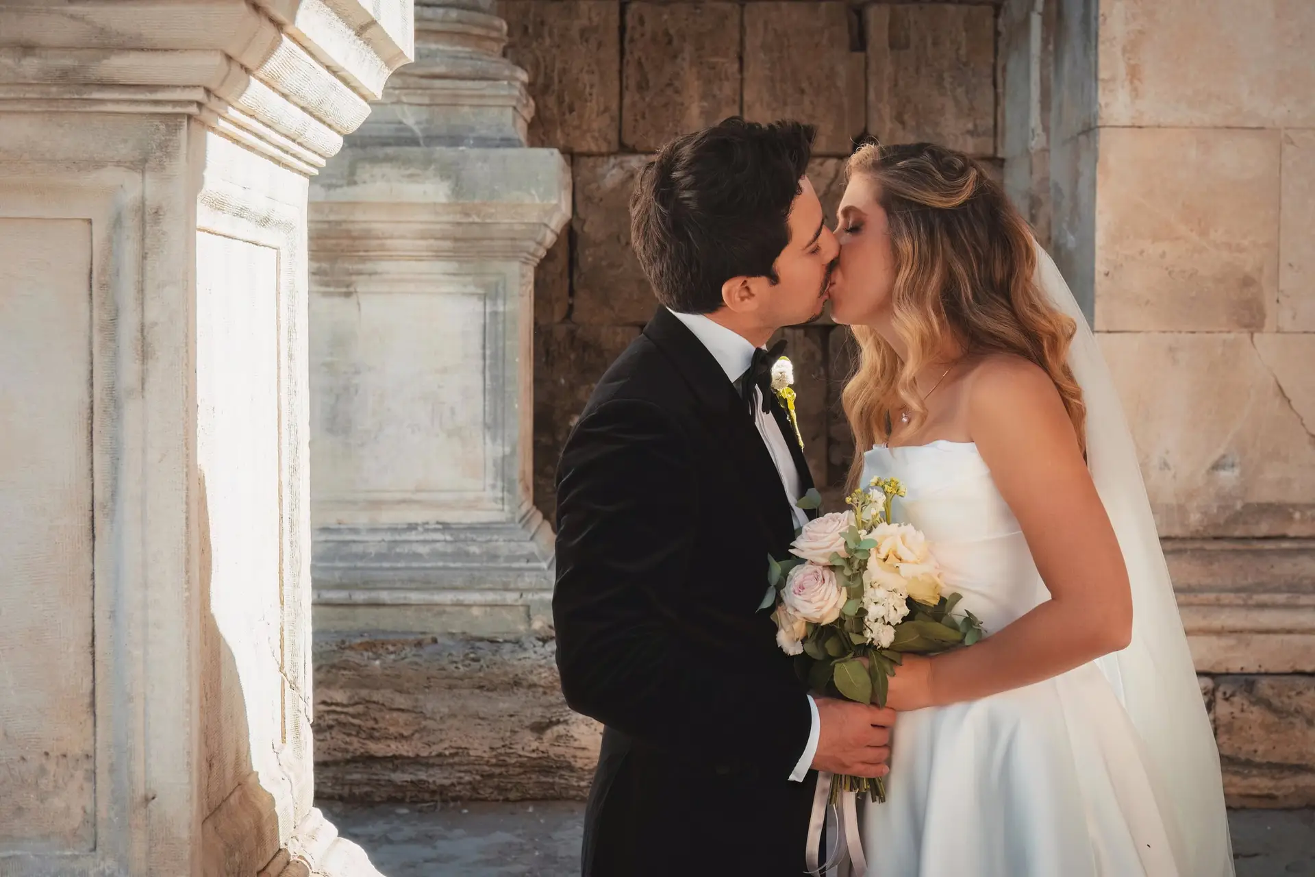 Bride and groom kissing between marble columns