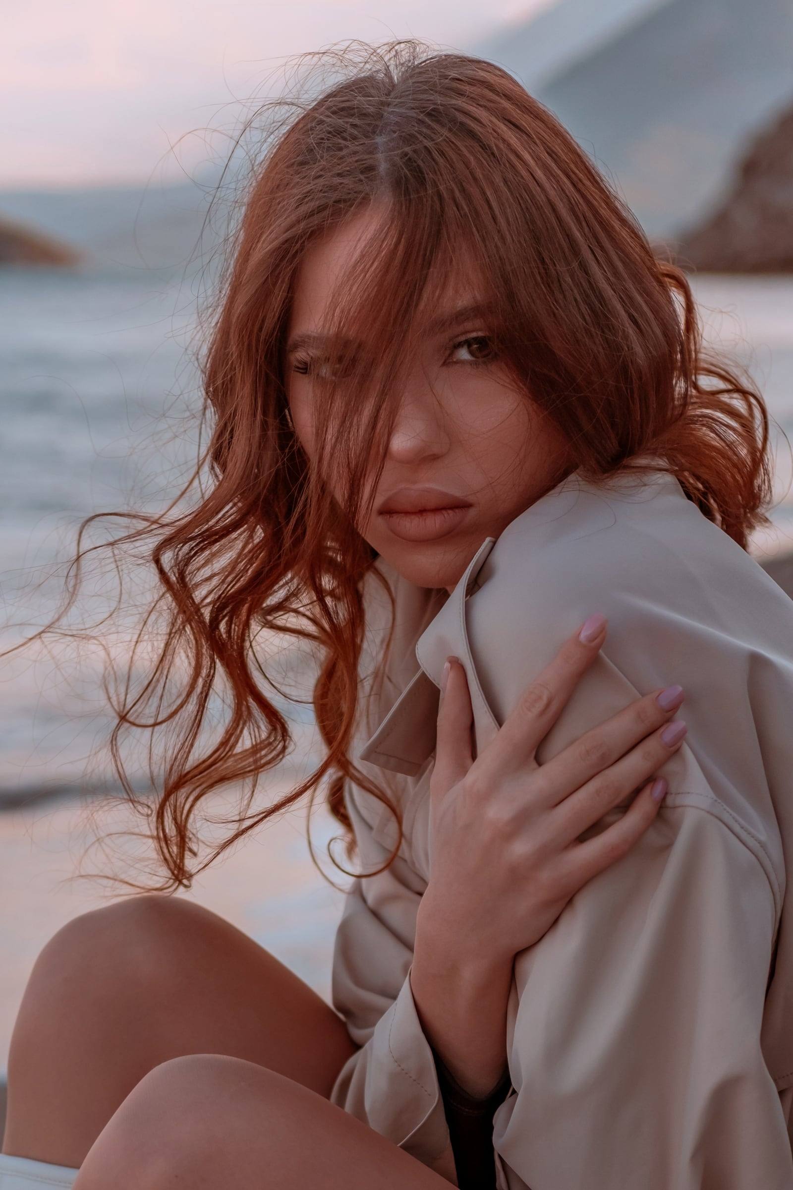 Red-haired woman wrapped in a coat on the beach